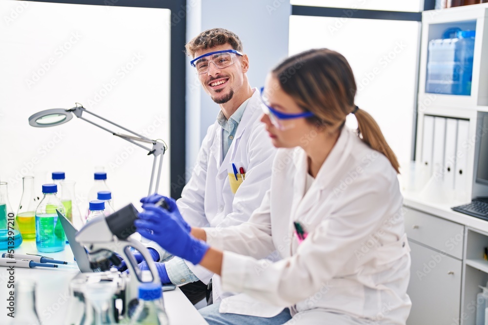 Young man and woman scientists workers using microscope at laboratory Young man and woman scientists workers using microscope at laboratory