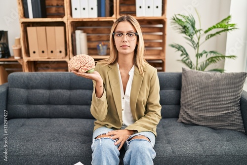 Fotografie Young blonde woman working at therapy office holding brain thinking attitude and