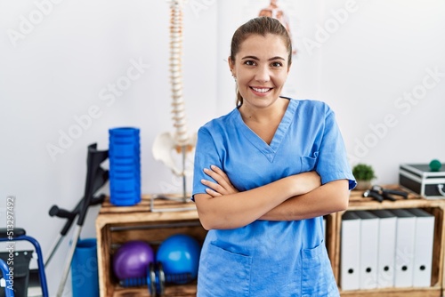 Young hispanic woman wearing physiotherapy uniform standing with arms crossed gesture at sport center