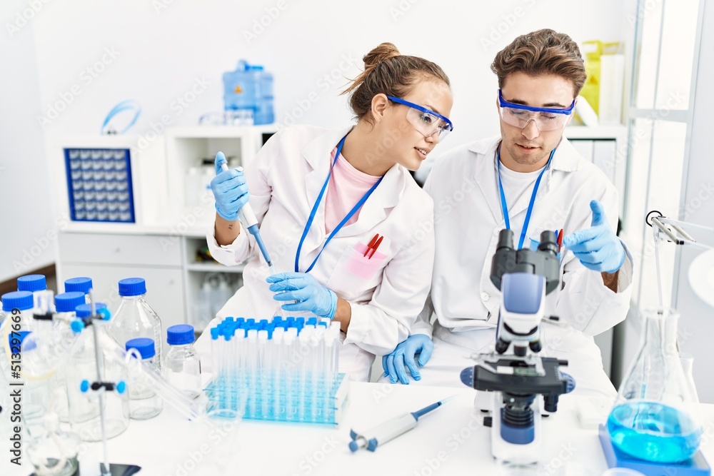 Man and woman wearing scientist uniform using pipette and microscope working at laboratory Man and woman wearing scientist uniform using pipette and microscope working at laboratory