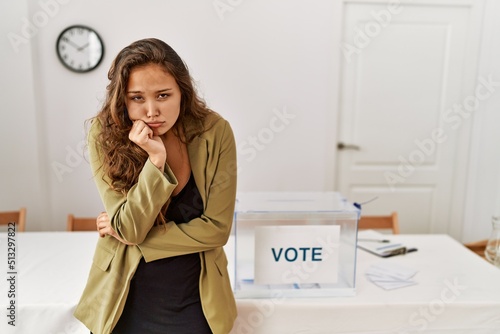 Beautiful hispanic woman standing at political campaign room thinking looking tired and bored with depression problems with crossed arms.