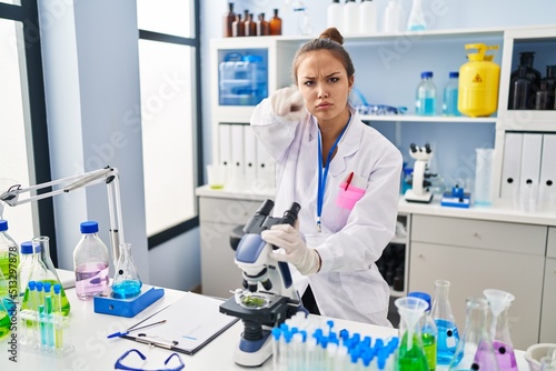 Young hispanic woman working at scientist laboratory pointing with finger to the camera and to you  confident gesture looking serious