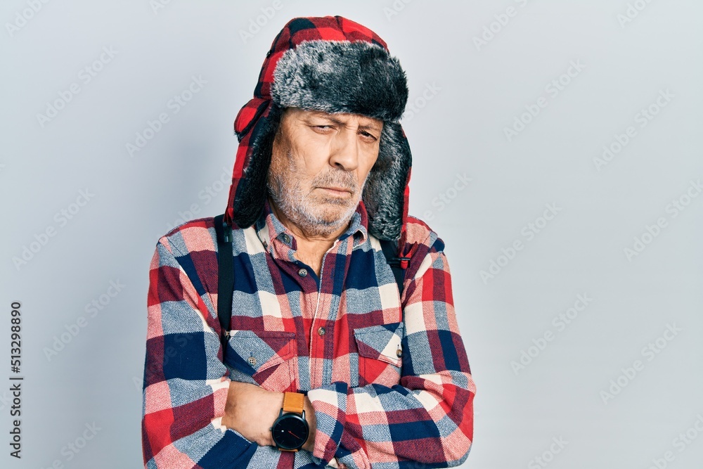 Handsome mature man wearing winter hat with ear flaps skeptic and nervous, disapproving expression on face with crossed arms. negative person. Handsome mature man wearing winter hat with ear flaps skeptic and nervous, disapproving expression on face with crossed arms. negative person.