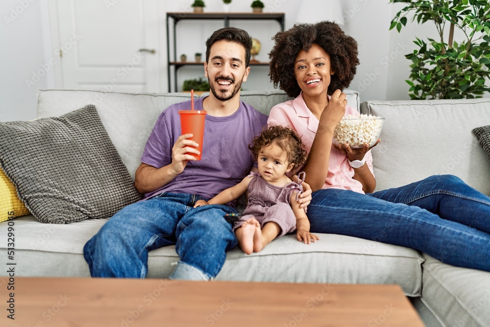 Couple and daughter watching movie sitting on sofa at home