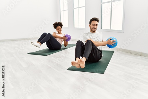 Young african american woman and hispanic man exercising at pilates room, stretching body and doing yoga pose, training strength and balance