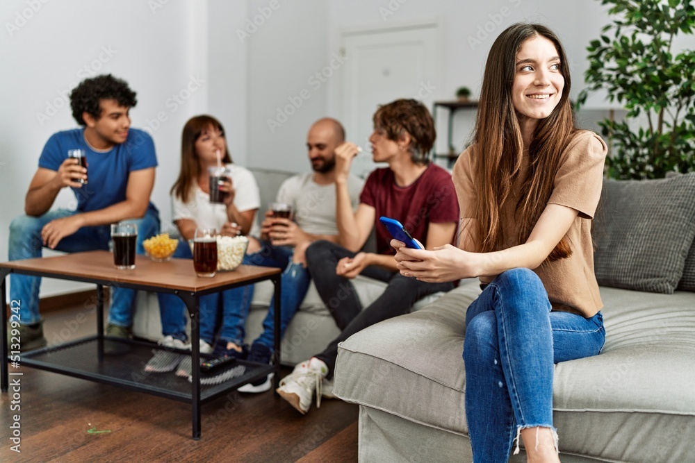 Group of young friends having party sitting on the sofa at home. Woman smiling happy using smartphone at home. Group of young friends having party sitting on the sofa at home. Woman smiling happy using smartphone at home.