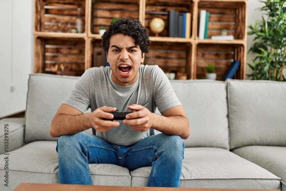 Young hispanic man playing video game sitting on the sofa at home. Young hispanic man playing video game sitting on the sofa at home.