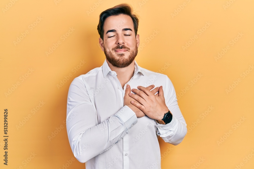 Handsome caucasian man with beard wearing business white shirt smiling with hands on chest, eyes closed with grateful gesture on face. health concept. Handsome caucasian man with beard wearing business white shirt smiling with hands on chest, eyes closed with grateful gesture on face. health concept.