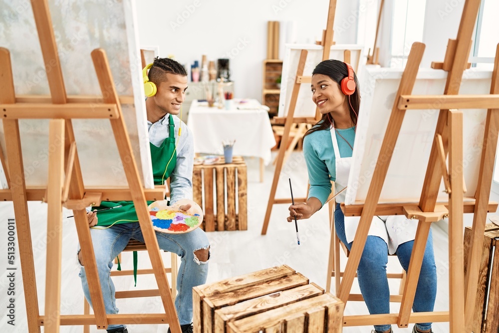 Young latin painter couple smiling happy painting and using headphones at art studio Young latin painter couple smiling happy painting and using headphones at art studio