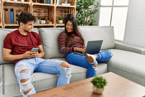 Young latin couple smiling happy using laptop and smartphone at home.