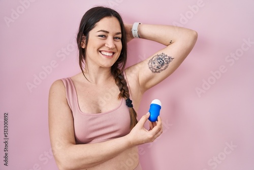 Young brunette woman using roll on deodorant smiling with a happy and cool smile on face. showing teeth.