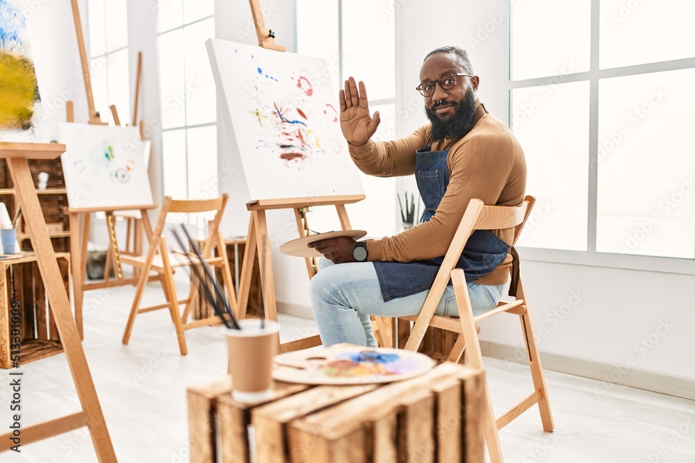 African american artist man painting on canvas at art studio with open hand doing stop sign with serious and confident expression, defense gesture