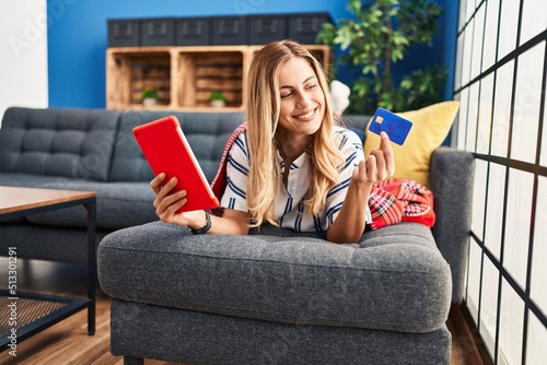 Young blonde woman using laptop and credit card sitting on sofa at home