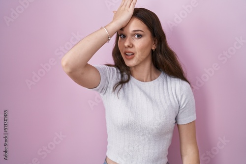 Young hispanic girl standing over pink background surprised with hand on head for mistake  remember error. forgot  bad memory concept.
