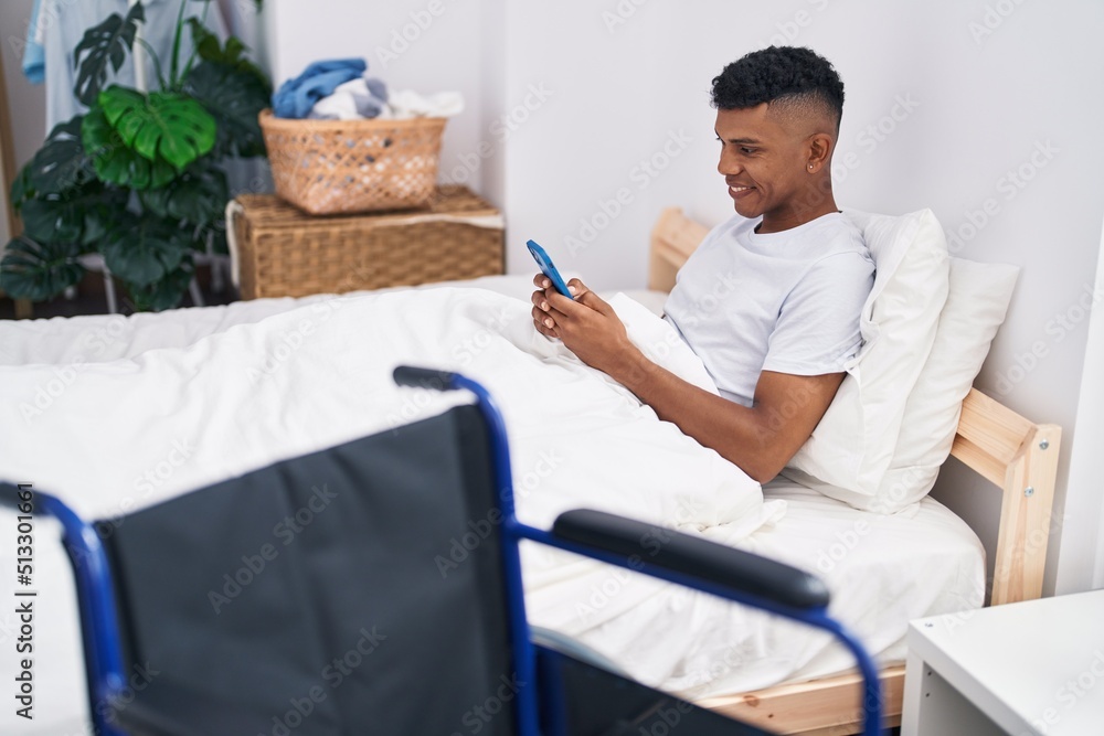 Obraz premium Young latin man using smartphone lying on bed at bedroom