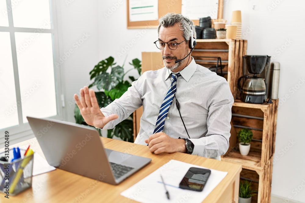 Middle age hispanic business man working at the office wearing operator headset doing stop sing with palm of the hand. warning expression with negative and serious gesture on the face. Middle age hispanic business man working at the office wearing operator headset doing stop sing with palm of the hand. warning expression with negative and serious gesture on the face.