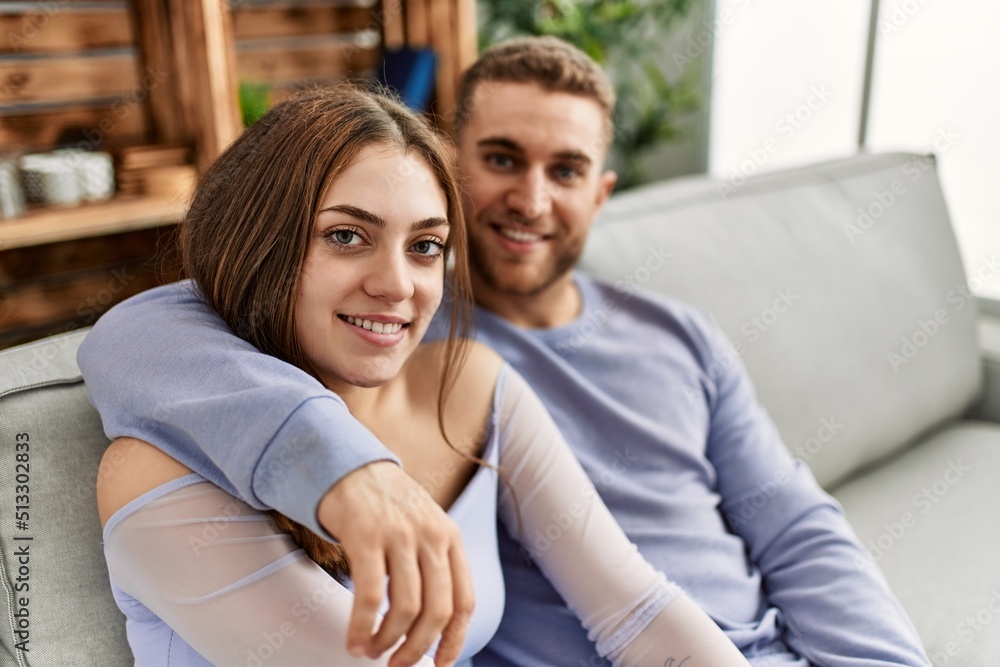 Young caucasian couple sitting on the sofa hugging at home.