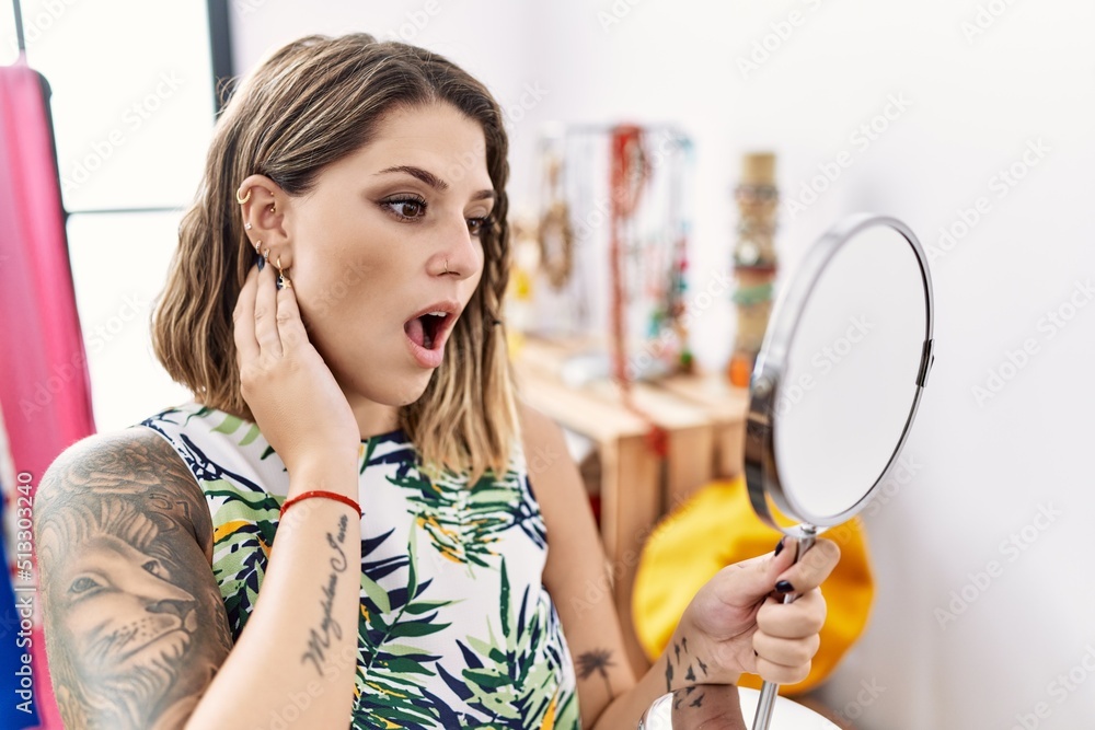 Young hispanic customer woman looking earrings on the mirror at store scared and amazed with open mouth for surprise, disbelief face Young hispanic customer woman looking earrings on the mirror at store scared and amazed with open mouth for surprise, disbelief face