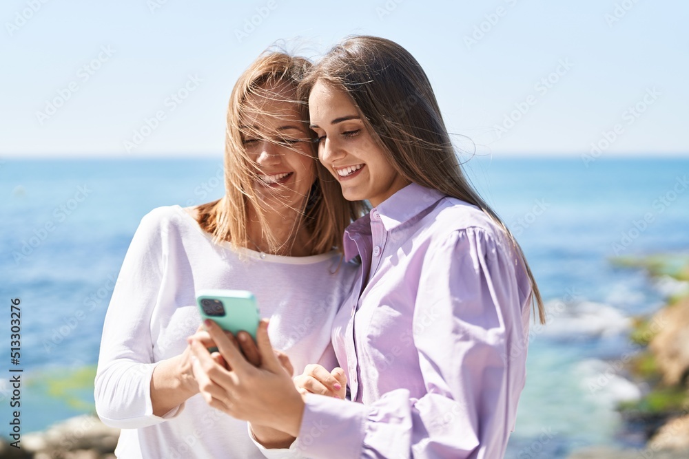 Two women mother and daughter using smartphone at seaside