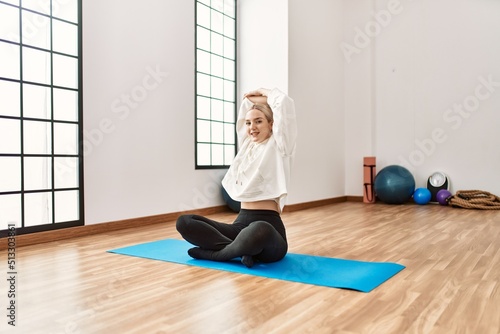 Young blonde girl smiling happy stretching at sport center.