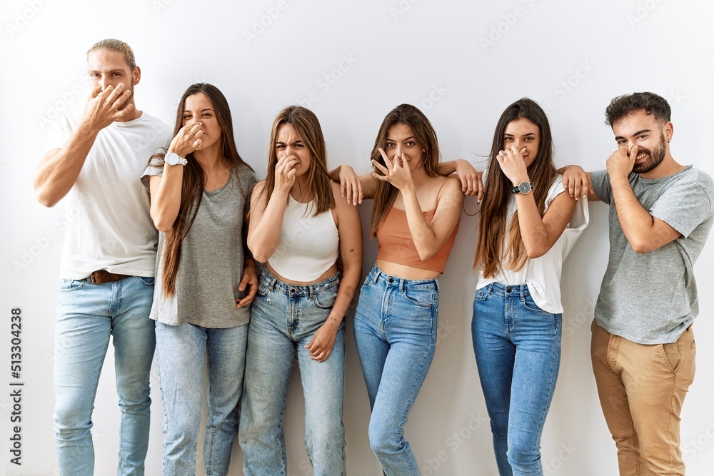 Group of young friends standing together over isolated background smelling something stinky and disgusting, intolerable smell, holding breath with fingers on nose. bad smell Group of young friends standing together over isolated background smelling something stinky and disgusting, intolerable smell, holding breath with fingers on nose. bad smell