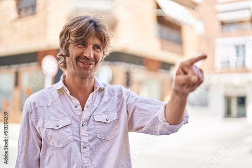 Young man smiling confident pointing with finger at street photo