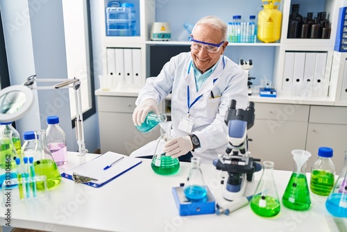 Senior man wearing scientist uniform pouring liquid at laboratory