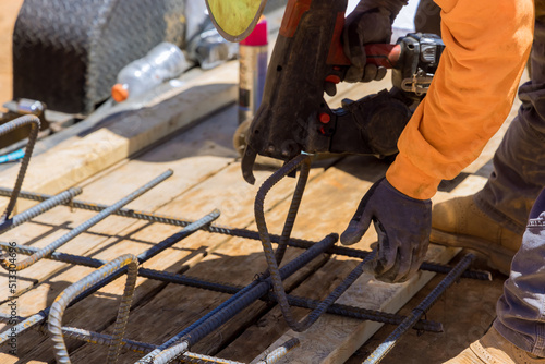 Using a rebar tying tool, construction worker twists steel bars with wire rods reinforcement for cement foundation