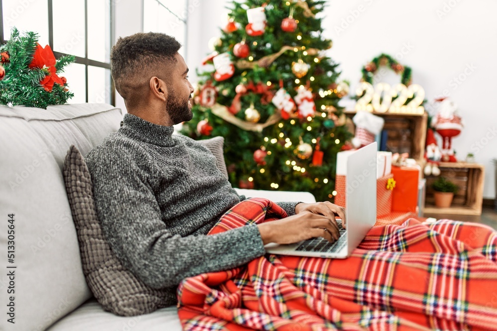Young african american man smiling happy using laptop sitting on the table at home. Young african american man smiling happy using laptop sitting on the table at home.
