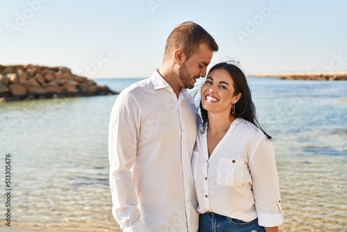 Man and woman couple smiling happy hugging each other standing at seaside