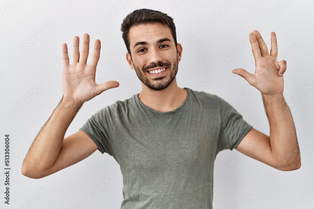 Young hispanic man with beard wearing casual t shirt over white background showing and pointing up with fingers number nine while smiling confident and happy. Young hispanic man with beard wearing casual t shirt over white background showing and pointing up with fingers number nine while smiling confident and happy.