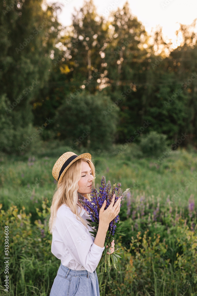 Beautiful dreamy girl in a straw hat sensually enjoying the scent of purple lupins Beautiful dreamy girl in a straw hat sensually enjoying the scent of purple lupins