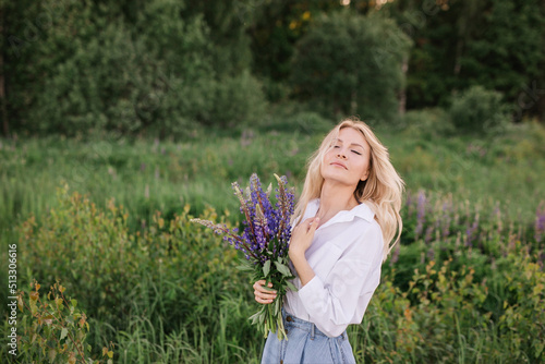 Close-up portrait of a relaxed sensual girl with a bouquet of purple lupins in rural greenery
