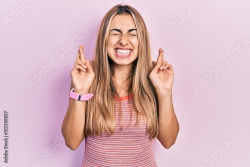 Beautiful hispanic woman wearing casual summer t shirt gesturing finger crossed smiling with hope and eyes closed. luck and superstitious concept.