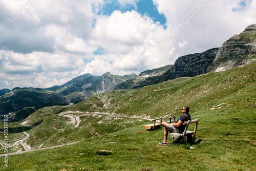 Single millenial man sits on a bench on a mountain plateau and looks at the mountains in front of him. Montenegro, Durmitor. Traveling solo