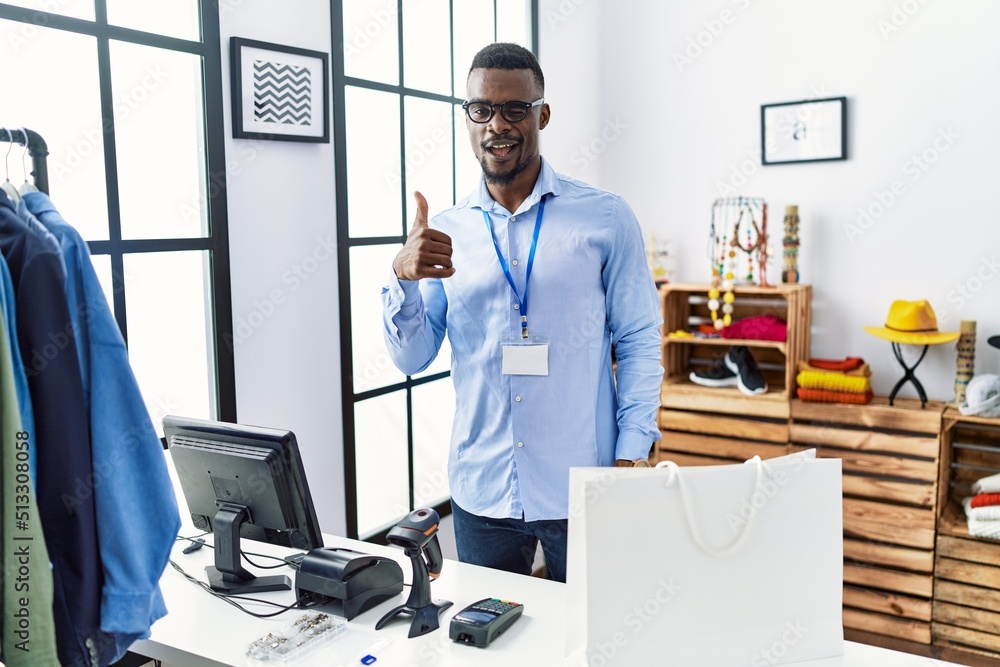 Young african man working as manager at retail boutique doing happy thumbs up gesture with hand. approving expression looking at the camera showing success. Young african man working as manager at retail boutique doing happy thumbs up gesture with hand. approving expression looking at the camera showing success.