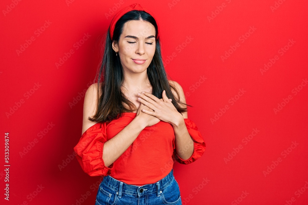 Young brunette woman wearing casual red shirt smiling with hands on chest, eyes closed with grateful gesture on face. health concept. Young brunette woman wearing casual red shirt smiling with hands on chest, eyes closed with grateful gesture on face. health concept.