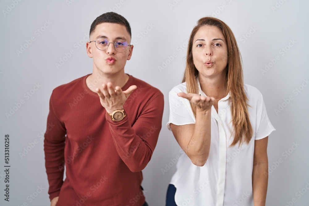 Mother and son standing together over isolated background looking at the camera blowing a kiss with hand on air being lovely and sexy. love expression. Mother and son standing together over isolated background looking at the camera blowing a kiss with hand on air being lovely and sexy. love expression.
