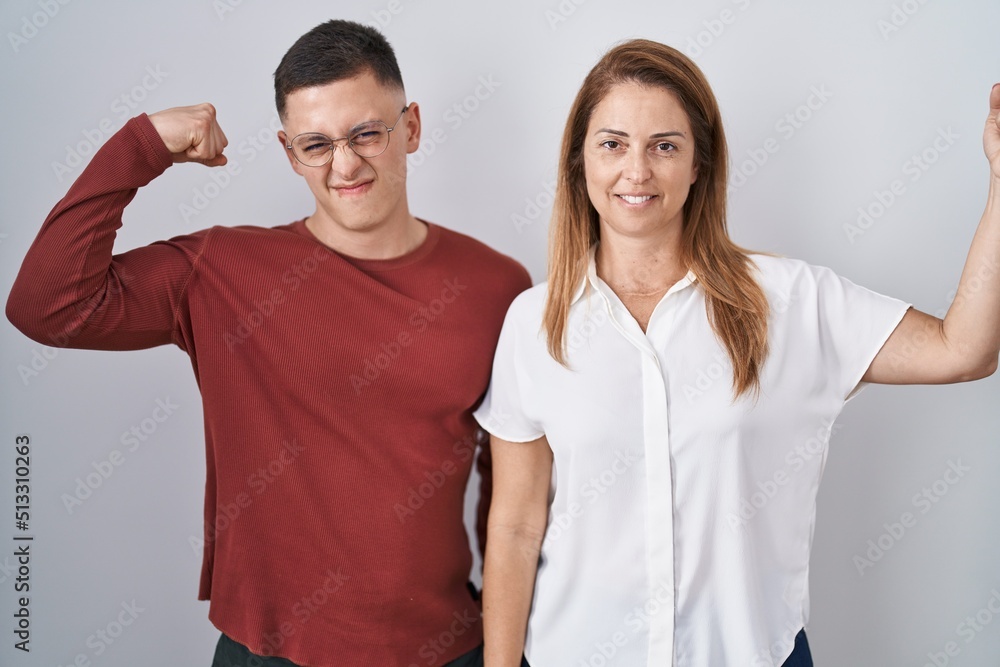 Mother and son standing together over isolated background strong person showing arm muscle, confident and proud of power Mother and son standing together over isolated background strong person showing arm muscle, confident and proud of power