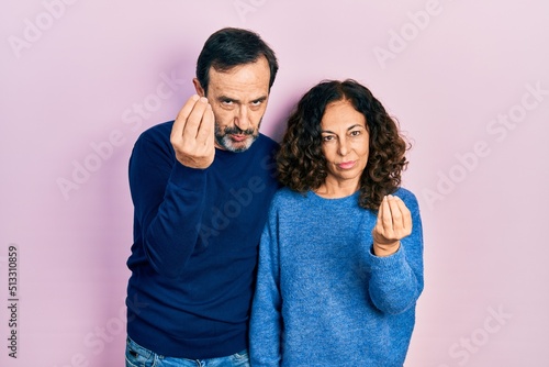 Middle age couple of hispanic woman and man hugging and standing together doing italian gesture with hand and fingers confident expression