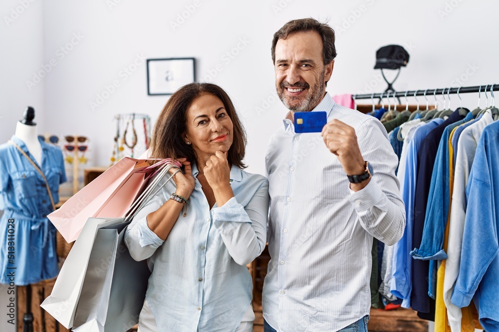 Hispanic middle age couple holding shopping bags and credit card looking confident at the camera smiling with crossed arms and hand raised on chin. thinking positive. Hispanic middle age couple holding shopping bags and credit card looking confident at the camera smiling with crossed arms and hand raised on chin. thinking positive.