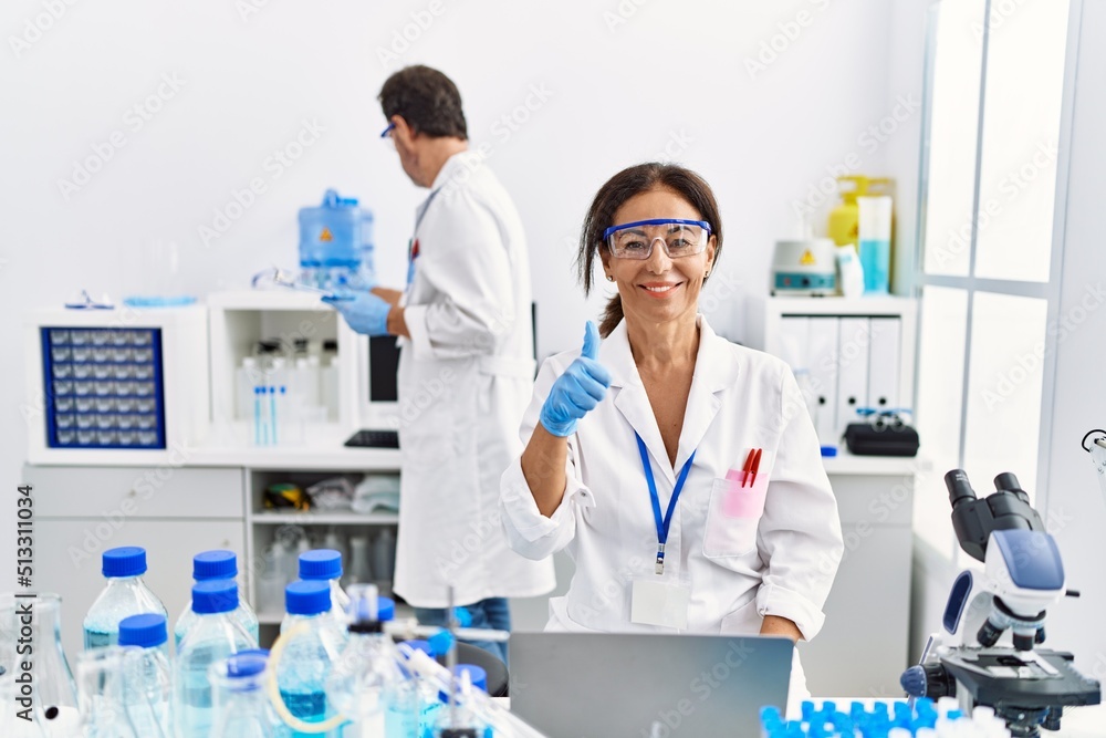 Middle age woman working at scientist laboratory smiling happy and positive, thumb up doing excellent and approval sign Middle age woman working at scientist laboratory smiling happy and positive, thumb up doing excellent and approval sign