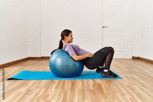 Young latin woman doing abs exercise using fit ball at sport center