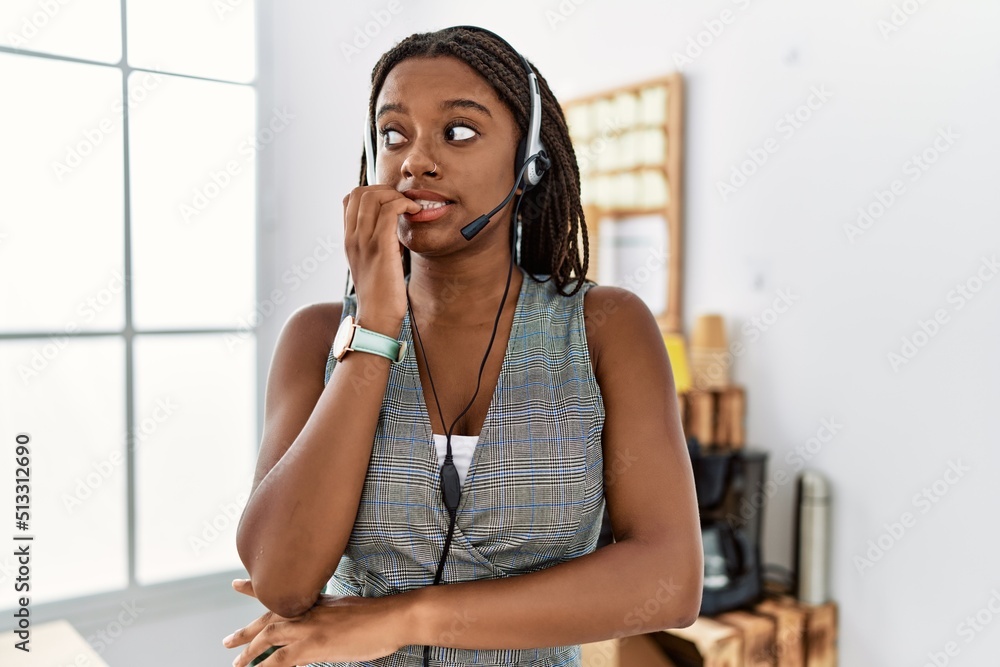 Naklejka premium Young african american woman working at the office wearing operator headset looking stressed and nervous with hands on mouth biting nails. anxiety problem.