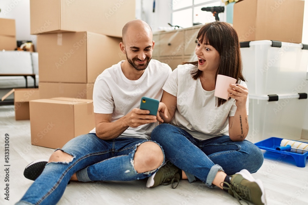 Young hispanic couple smiling happy using smartphone at new home. Young hispanic couple smiling happy using smartphone at new home.