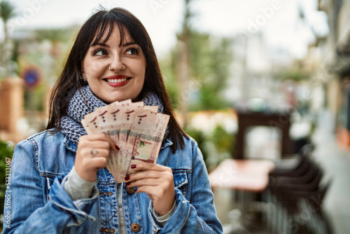 Young brunette woman holding arabia saudi riyal banknotes at the city photo