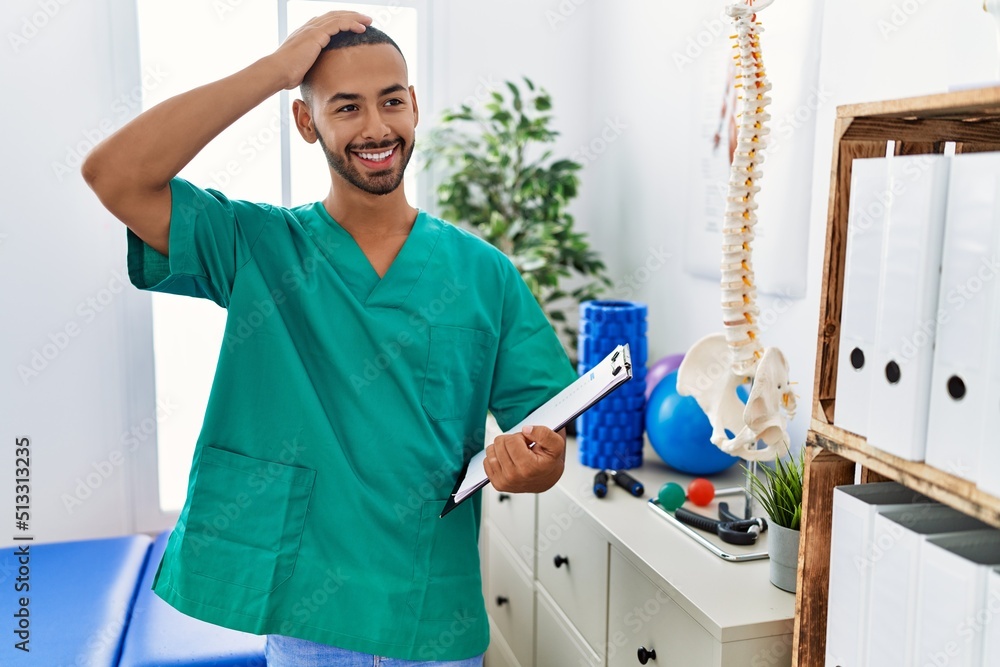 Fototapeta premium African american physiotherapist man working at pain recovery clinic smiling confident touching hair with hand up gesture, posing attractive and fashionable