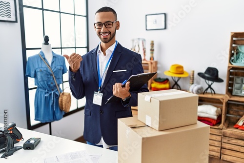 African american man working as manager at retail boutique pointing to the back behind with hand and thumbs up, smiling confident