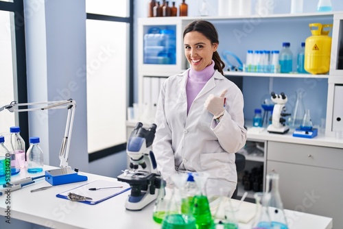 Young brunette woman working at scientist laboratory smiling happy and positive  thumb up doing excellent and approval sign