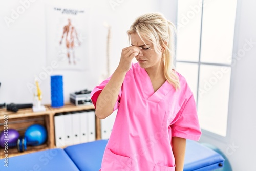 Young caucasian woman working at pain recovery clinic tired rubbing nose and eyes feeling fatigue and headache. stress and frustration concept.